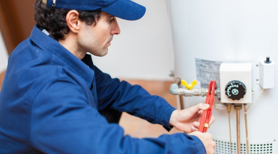 Plumber performing maintenance on a water heater, using tools to ensure optimal functioning and safety in home heating systems.